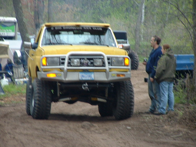 Lifted yellow Ford Bronco 4x4 with tube brush guard and mud tires on a dirt trail