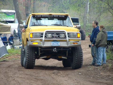 1988 Ford Bronco - A yellow off-road SUV is parked on a dirt path, with people standing nearby and other vehicles in the background.