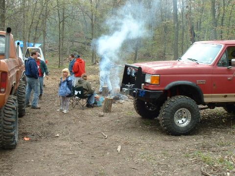 1988 Ford Bronco - A group of people are gathered around a campfire next to a red 1988 Ford Bronco.