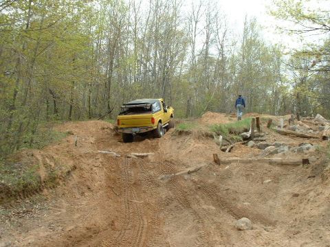 1988 Ford Bronco - A yellow SUV navigates a challenging dirt path in a wooded area.