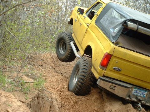 1988 Ford Bronco - This modified SUV is navigating a steep, muddy incline with its tires digging into the loose soil.