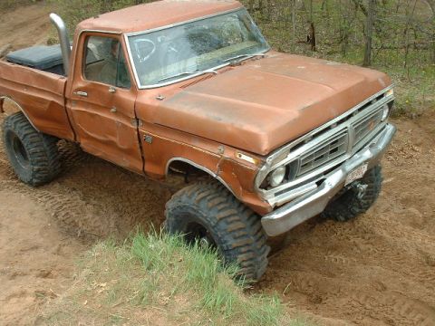 1988 Ford Bronco - This orange pickup truck, likely a 1973 model, is stuck in the dirt with its large tires digging in.