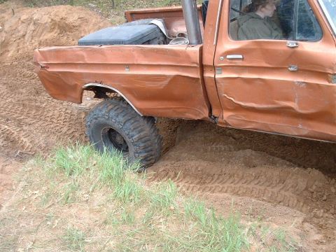 1988 Ford Bronco - This heavily damaged orange pickup truck appears to be from the 1970s and is stuck in the mud.