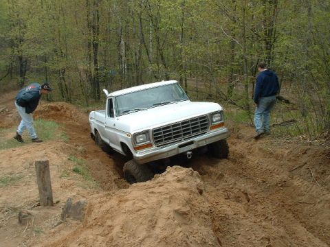 1988 Ford Bronco - A white pickup truck is shown off-roading on a dirt path with two people observing.