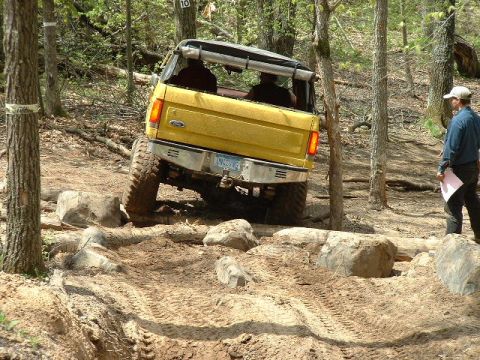 1988 Ford Bronco - A yellow SUV tackles a challenging off-road course with a person observing.