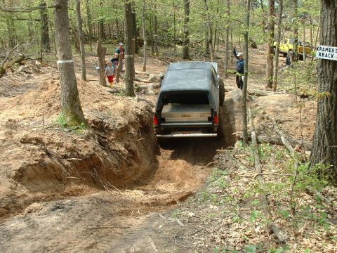 1988 Ford Bronco - An off-road vehicle navigates a challenging dirt path surrounded by trees and spectators.