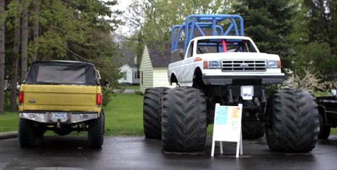 1988 Ford Bronco - A yellow Ford Bronco and a white monster truck are parked side-by-side outdoors.