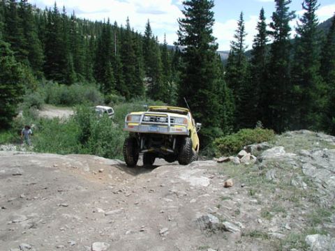 1988 Ford Bronco - A yellow 1988 Ford Bronco navigates a mountain trail, with another vehicle visible in the distance.
