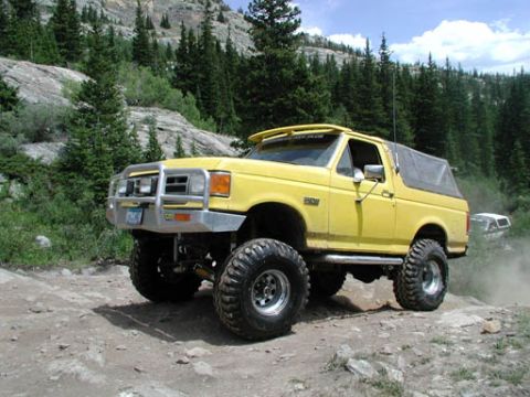 1988 Ford Bronco - Modified yellow Ford Bronco navigates a rocky mountain trail with a second vehicle visible in the distance.