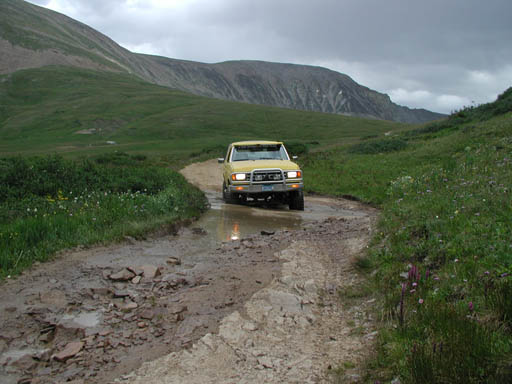 Yellow pickup truck driving through a muddy mountain road puddle