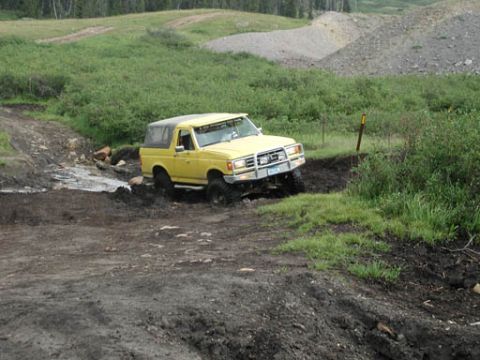 1988 Ford Bronco - A yellow SUV tackles a challenging muddy off-road course.
