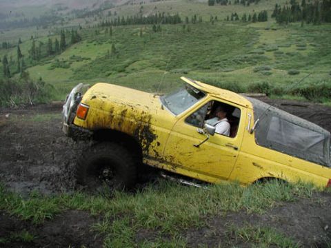1988 Ford Bronco - A yellow Ford Bronco is stuck in thick mud on a grassy, hilly terrain.