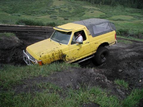 1988 Ford Bronco - A yellow 1987 Ford Bronco navigates a muddy off-road course, its tires deep in the muck.