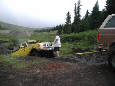 1988 Ford Bronco - Two Ford Broncos navigate muddy terrain, one vehicle assisting the other out of a deep mud pit.
