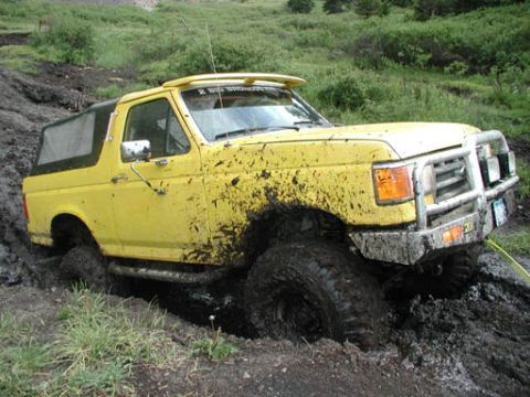 1988 Ford Bronco - This off-road vehicle is deeply mired in thick mud, with its tires submerged.