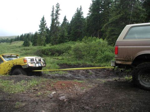 1988 Ford Bronco - Two SUVs are stuck in the mud, with one vehicle being towed out by the other.