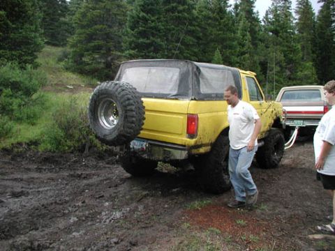 1988 Ford Bronco - Yellow 1988 Ford Bronco with soft top and spare tire on rear, parked in mud.