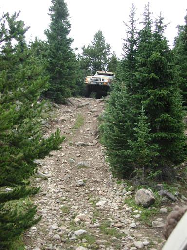 1988 Ford Bronco - A vehicle navigates a challenging, unpaved trail surrounded by dense forest.
