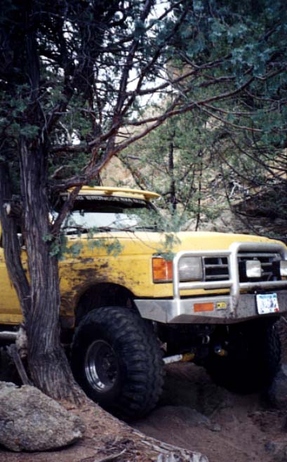 1988 Ford Bronco - A yellow 1989 Ford Bronco navigates rough terrain, its front end angled towards the viewer.