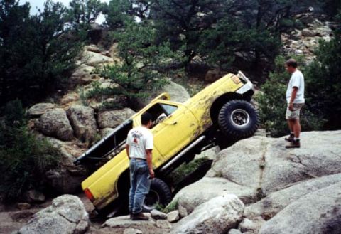1988 Ford Bronco - Off-road pickup truck navigating difficult rocky terrain with two people watching.
