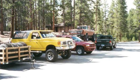1988 Ford Bronco - Several trucks, including a lifted yellow Ford Bronco, are parked in a wooded area.