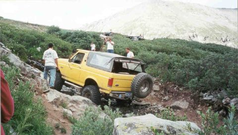 1988 Ford Bronco - This yellow SUV is navigating a steep, rocky incline with several people observing the action.