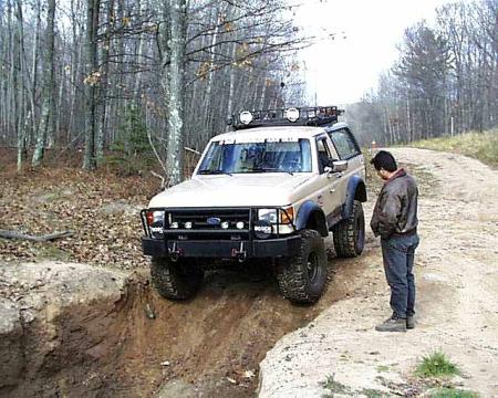 1988 Ford Bronco - A tan 1987 Ford Bronco is shown navigating a challenging off-road terrain with a person observing.