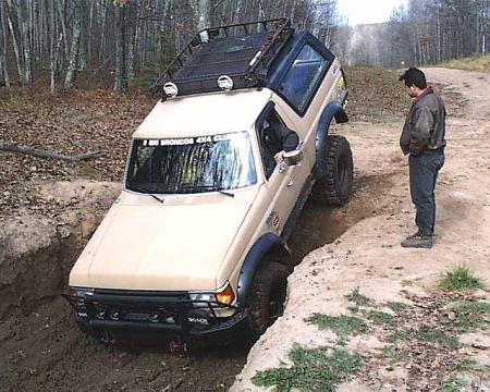 1988 Ford Bronco - 1988 Ford Bronco navigates a challenging off-road obstacle on a wooded trail.