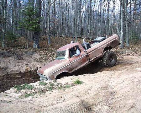 1988 Ford Bronco - A man drives a rusty pickup truck through a wooded area, getting stuck in a ditch.