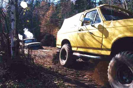 1988 Ford Bronco - A yellow SUV navigates a muddy trail while another vehicle appears stuck in the background.