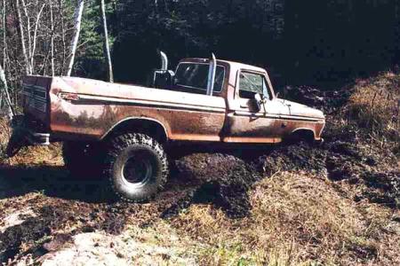 1988 Ford Bronco - This pickup truck appears to be from the 1970s and is stuck in a muddy, wooded area.