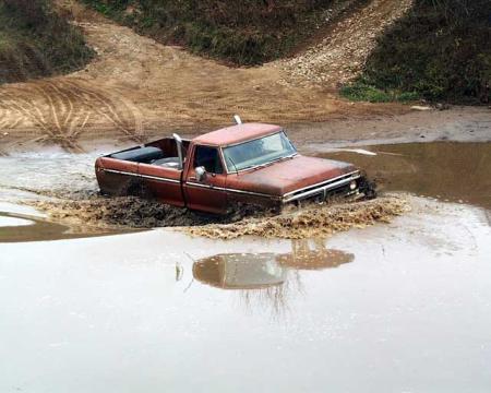 1988 Ford Bronco - Pickup truck struggles through deep mud and water, wheels submerged.