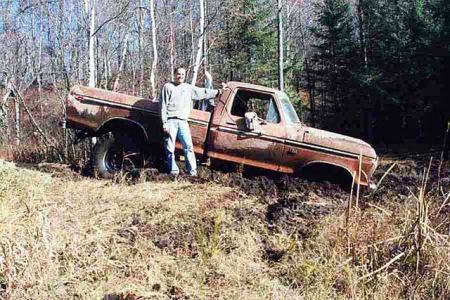 1988 Ford Bronco - A man poses with his stuck pickup truck in a muddy, wooded area.
