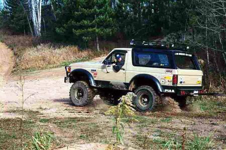 1988 Ford Bronco - This off-road vehicle navigates a wooded trail with a driver visible inside.