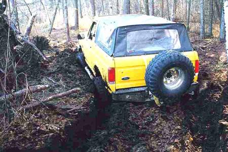 1988 Ford Bronco - 1988 Ford Bronco with soft top is stuck in mud on a wooded trail.