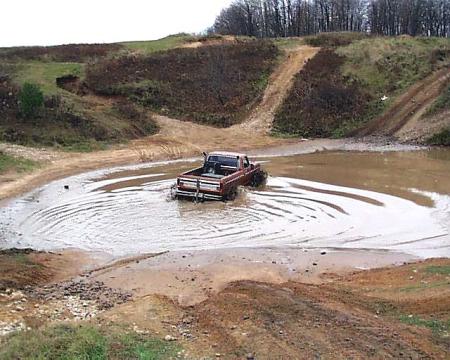 1988 Ford Bronco - A red pickup truck navigates a muddy off-road course.