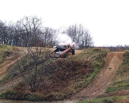 1988 Ford Bronco - A red pickup truck is seen on a dirt hill, with smoke emanating from its open hood.