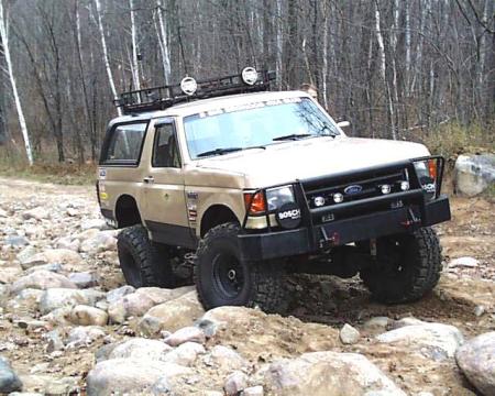1988 Ford Bronco - 1988 Ford Bronco tackling a challenging rocky path in a wooded area.