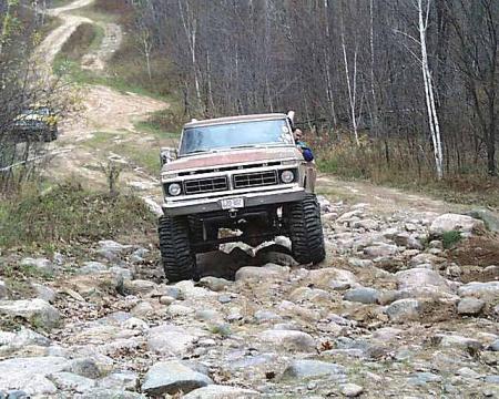 1988 Ford Bronco - This modified truck navigates a rocky off-road path with trees on either side.