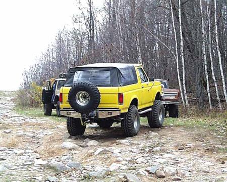 1988 Ford Bronco - A yellow 1987 Ford Bronco is parked on a rocky trail, with another vehicle visible behind it.