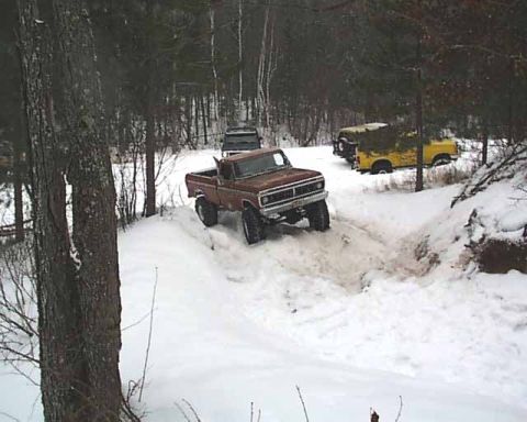1988 Ford Bronco - Several trucks navigate a snowy trail in a wooded area during winter.