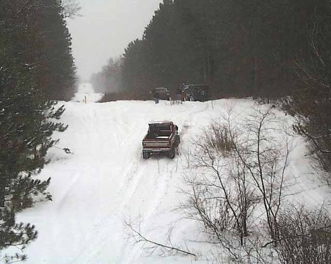 1988 Ford Bronco - Several vehicles navigate a snow-covered road through a wooded area.