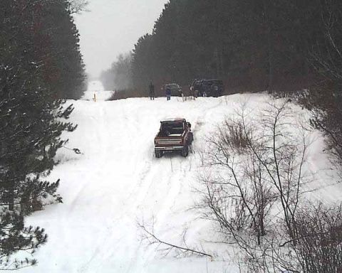 1988 Ford Bronco - Multiple vehicles navigate a snow-covered road surrounded by trees.