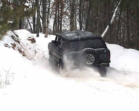 1988 Ford Bronco - A black SUV navigates a snowy trail, its tires churning through the slush.