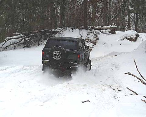 1988 Ford Bronco - 1988 Ford Bronco navigates a snowy trail, kicking up snow.