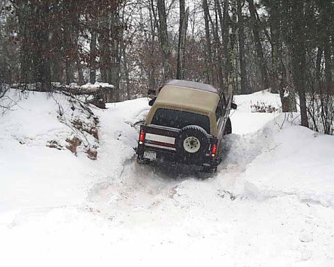 1988 Ford Bronco - A Ford Bronco navigates a snowy path in a wooded area during winter.