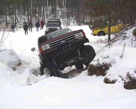1988 Ford Bronco - Maroon Ford Bronco attempts to drive through a snow-covered trail with other vehicles present.