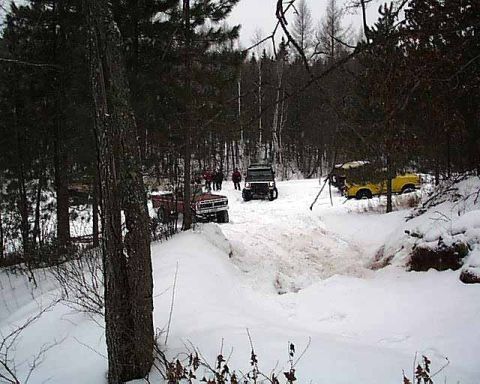 1988 Ford Bronco - Multiple vehicles are seen off-roading in a snowy forest environment during the winter.