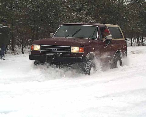 1988 Ford Bronco - 1988 Ford Bronco navigating a snowy terrain, with trees in the background.