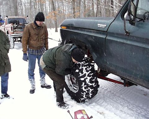 1988 Ford Bronco - A dark green 1988 Ford Bronco is partially visible as a person inspects its front tire in a snowy environment.